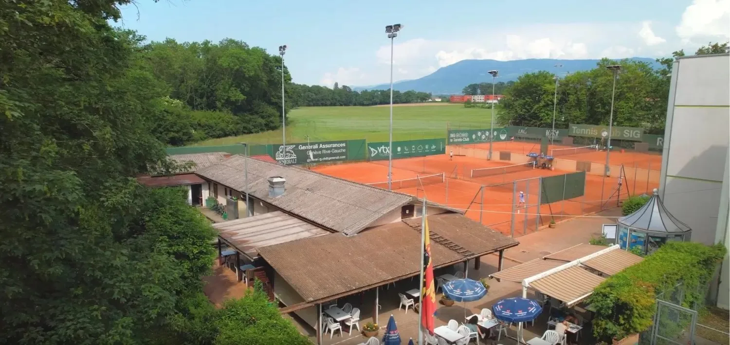 Le club-house et sa terrasse, les courts en terre battue et les montagnes, vus d’en haut