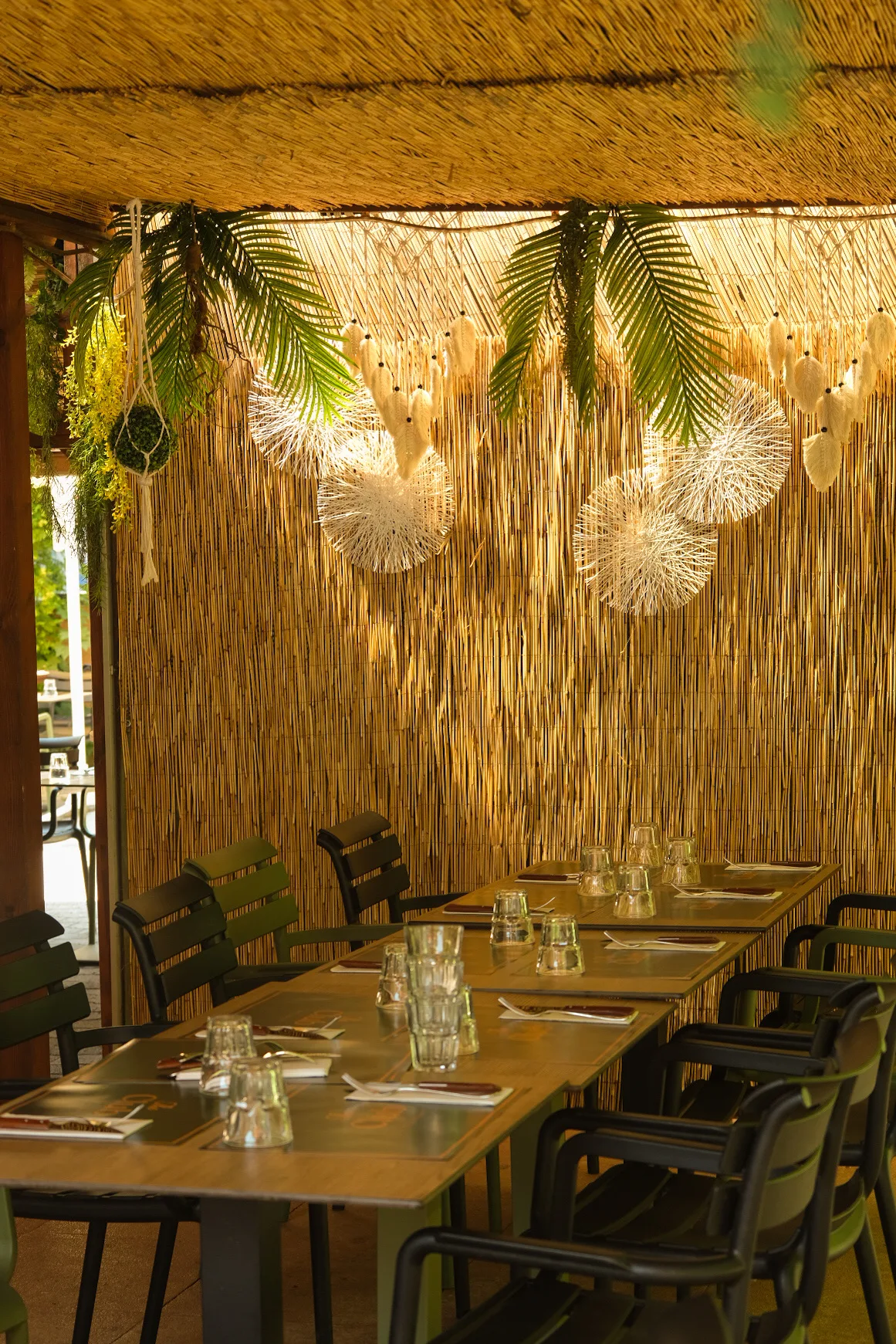 Les tables dressées sur la partie couverte de la terrasse, sous les canisses et les palmes