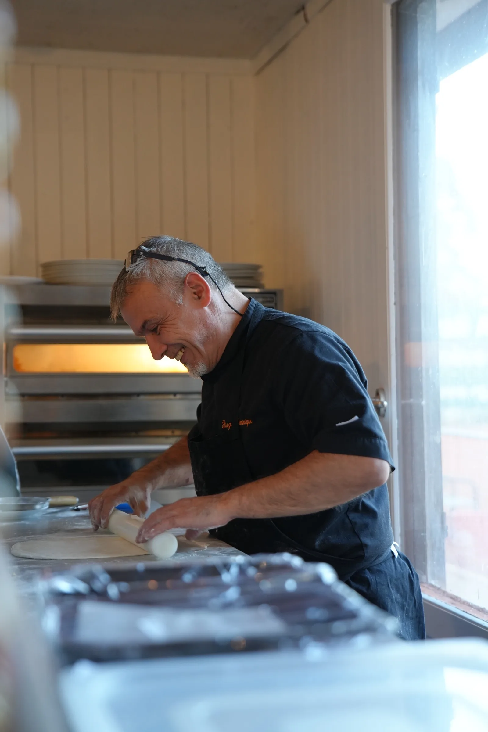 Le chef prépare une pizza, souriant, devant le four