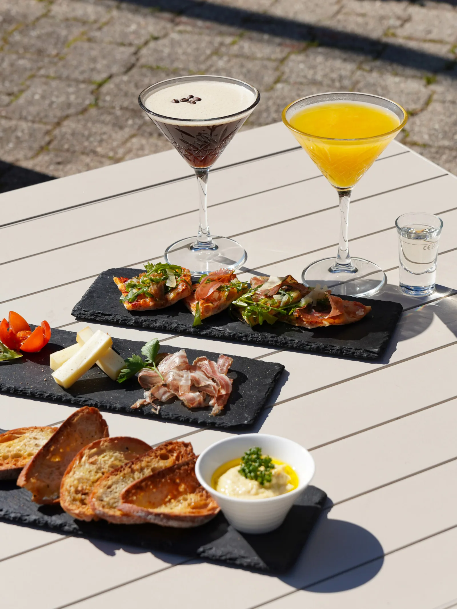 Planches à partager au soleil sur la terrasse : bruschettas, jambon cru, fromage, pain grillé et boissons